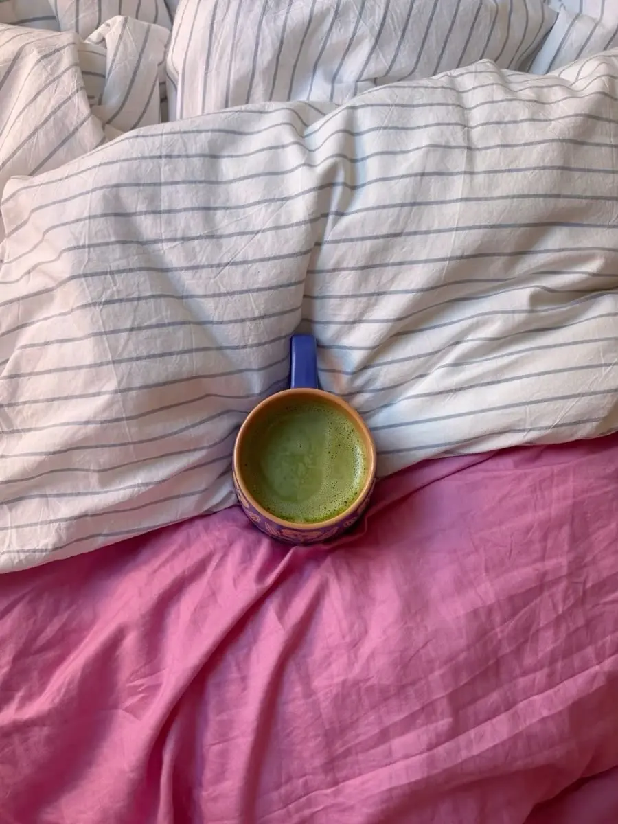 Cama con textiles rosados y una bebida verde