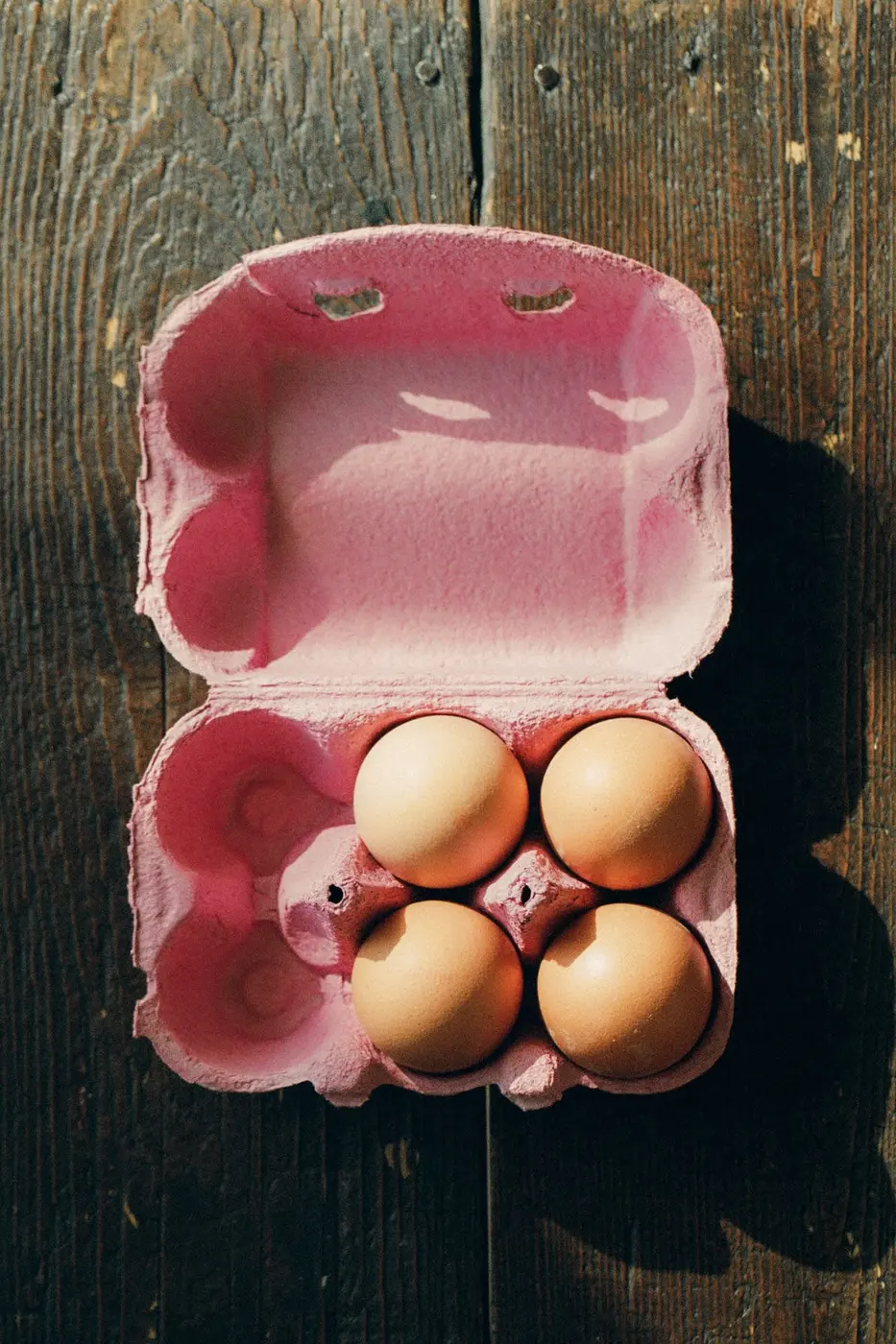 Huevos en una caja rosada sobre madera